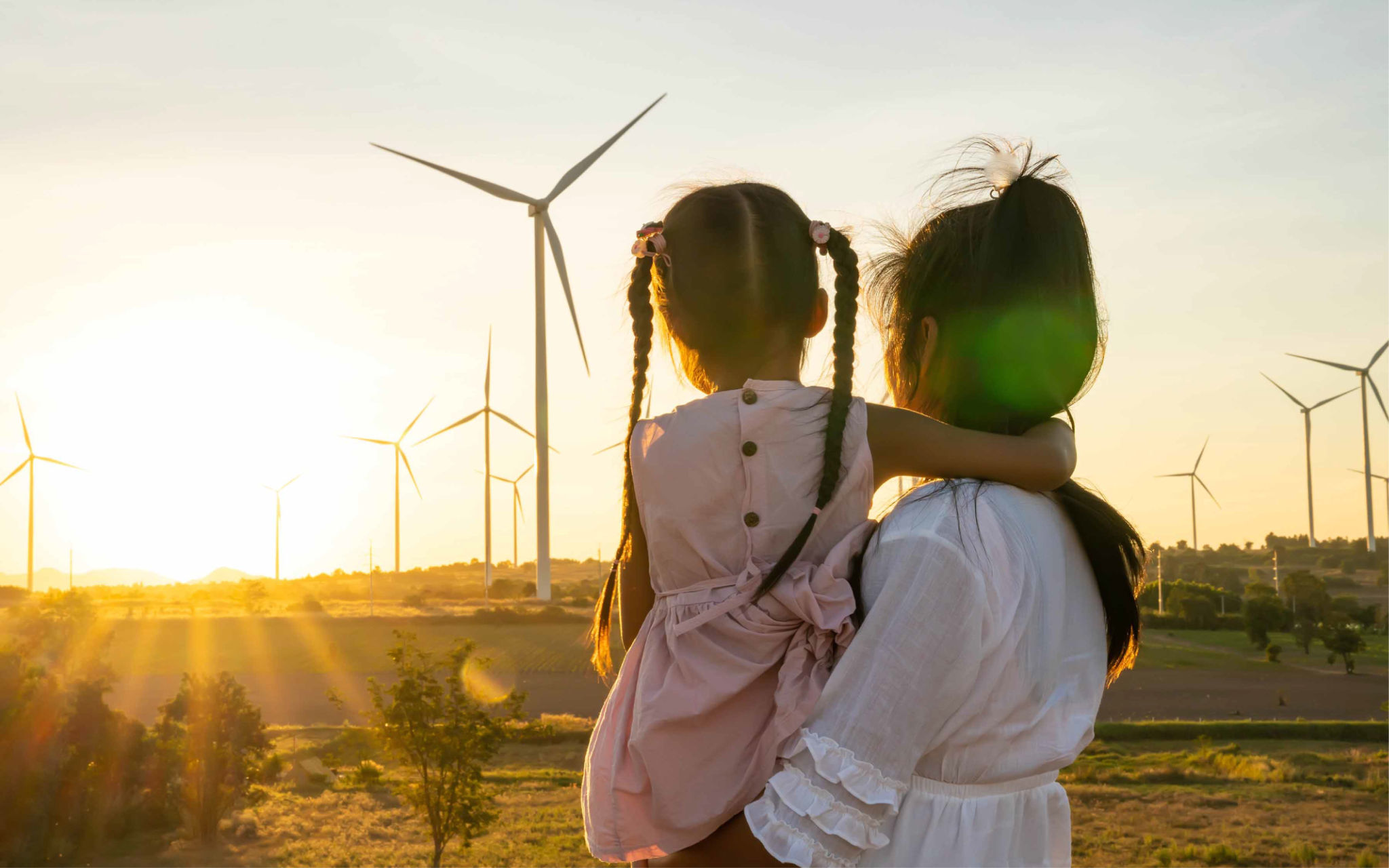 Woman holding child looking at sunset with windmills in the background.