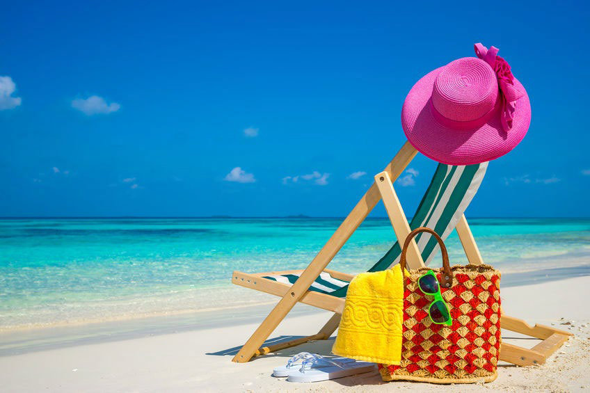Beach chair with a pink hat on it and a yellow bag next to it.