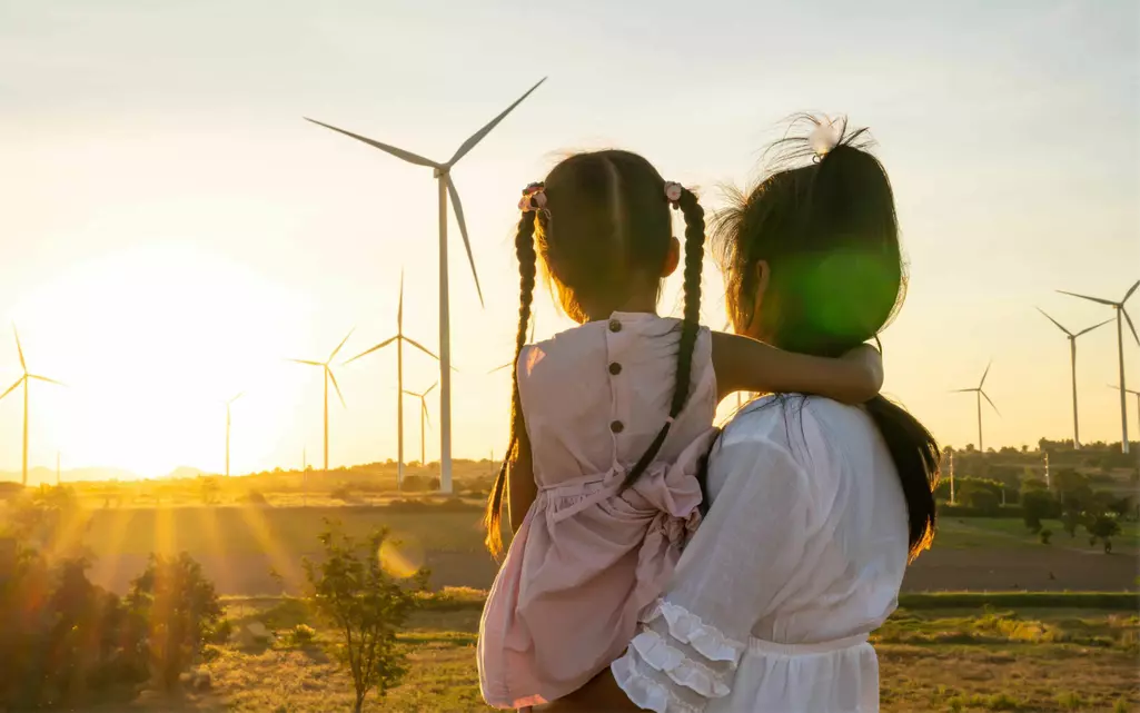 Woman holding child looking at sunset with windmills in the background.