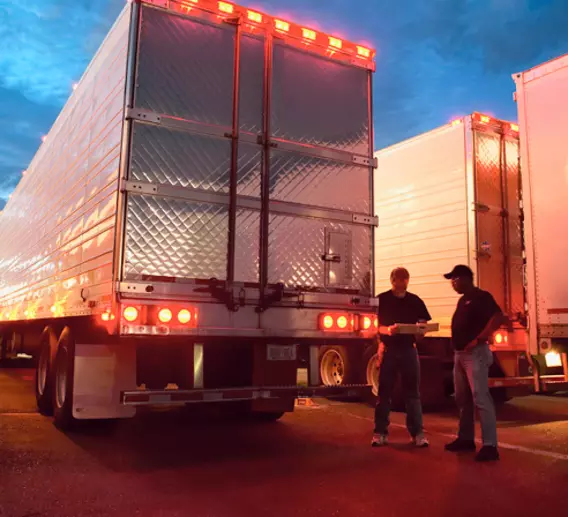 Team drivers stand outside of their truck in a parking lot