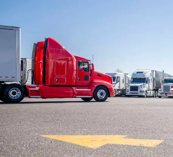 Red truck waiting in busy lot with many other trucks. 