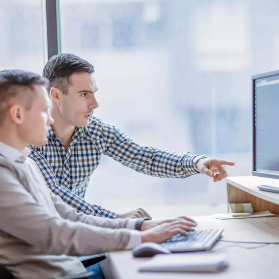 Two men sitting together at a computer while one points to their managed logistics plan on the screen.