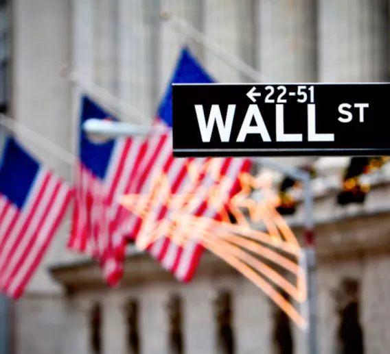 Street sign for "Wall St" in front of American flags.