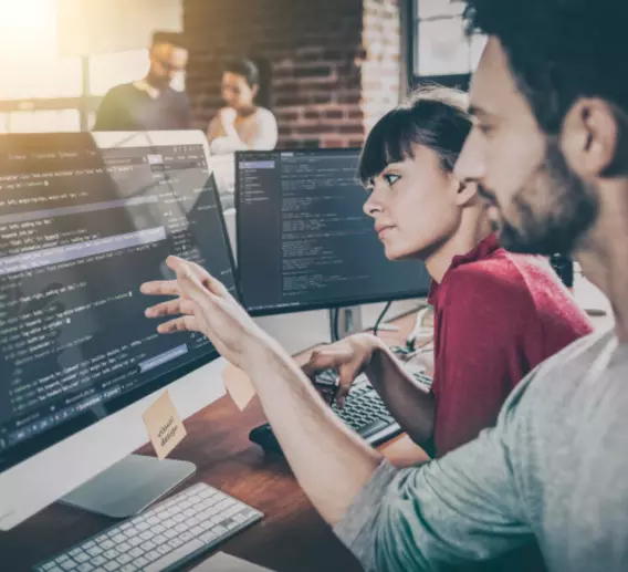 A man and woman look over code at a computer.