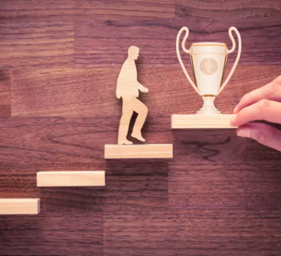 A silhouette of a man walking up steps to a large trophy.