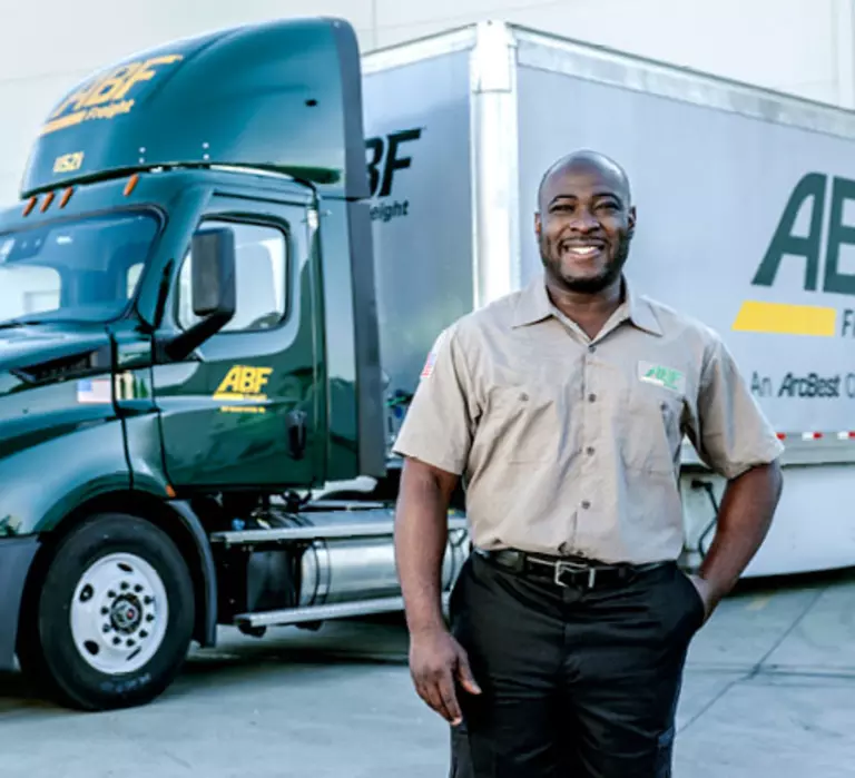 ABF driver stands in front of ABF truck in a parking lot.