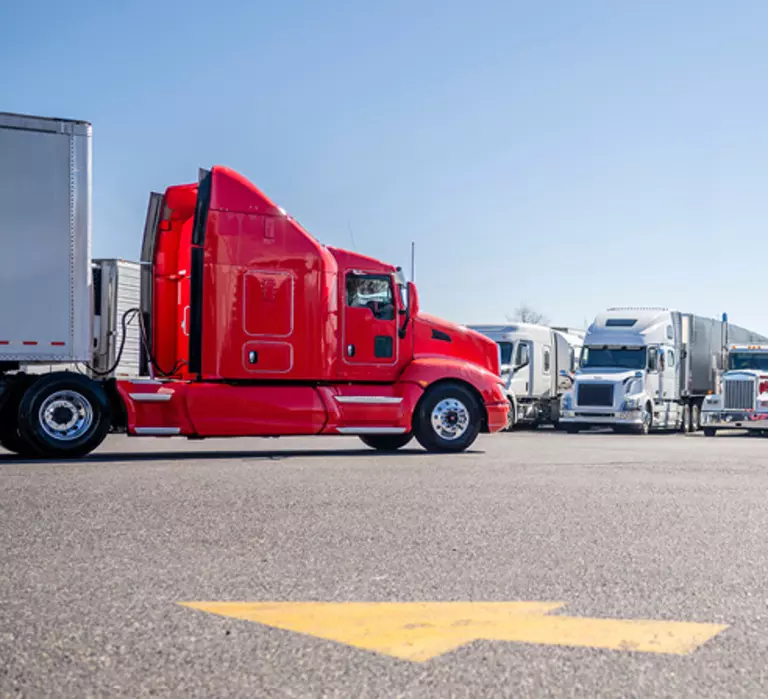 Red truck waiting in busy lot with many other trucks. 