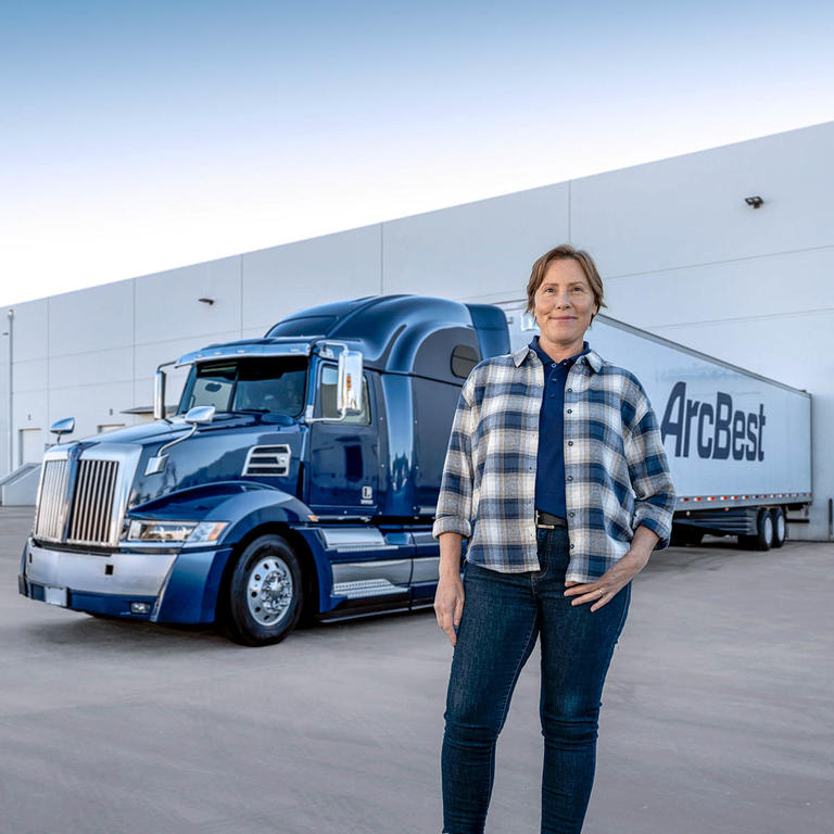 Female dedicated driver standing beside an ArcBest truck.