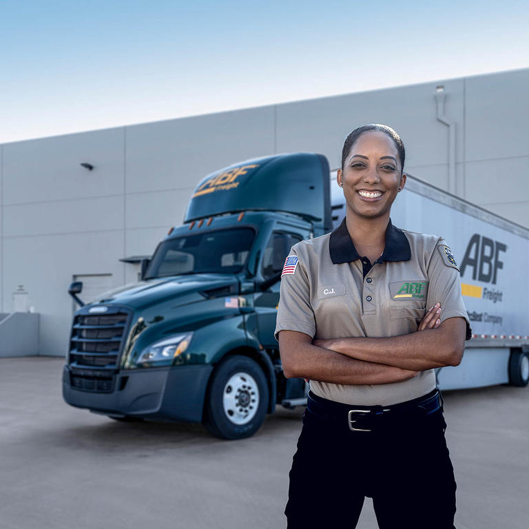 Female ABF Freight driver stands beside ABF truck.