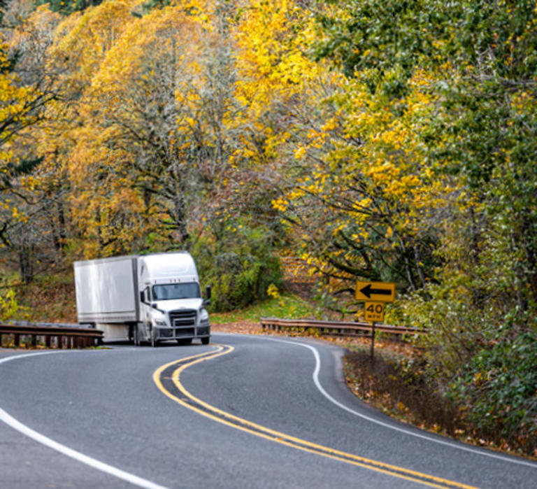 Semi truck driving around a curve surrounded by fall foliage.