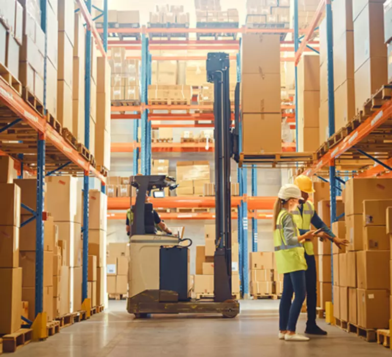 A man and woman standing in a warehouse in front of a forklift.