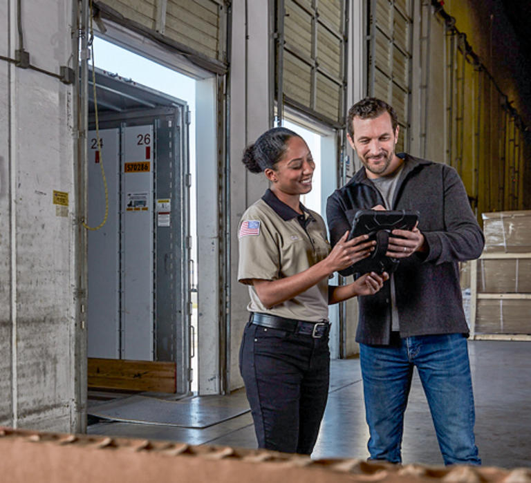 Female LTL driver discusses an LTL shipment with a male customer on a loading dock.