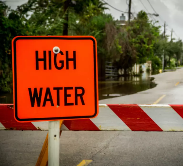 Partially flooded road with barricade and High Water sign.