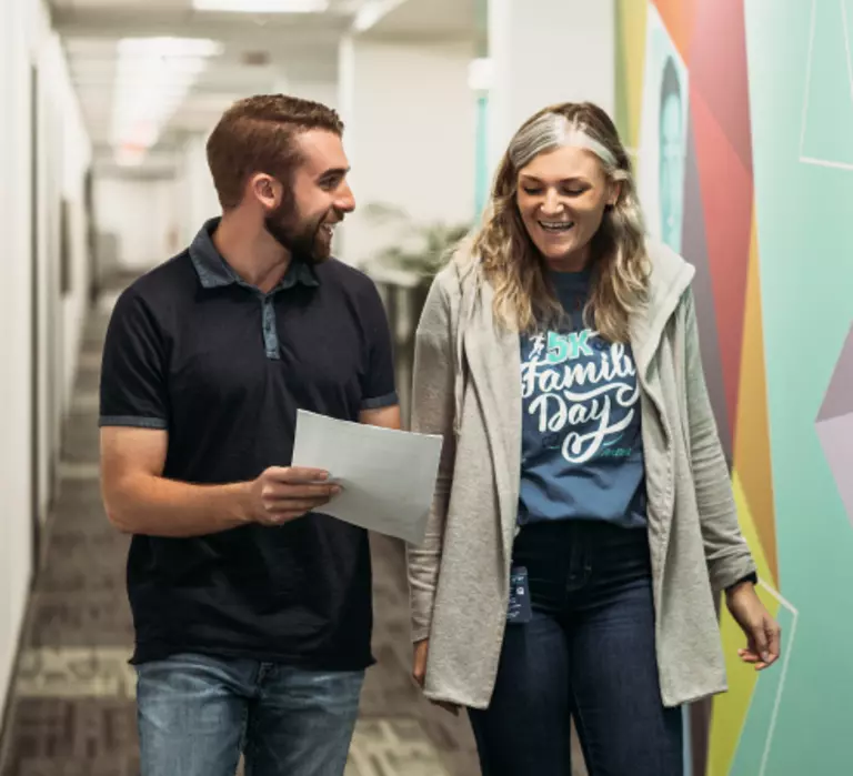 Two ArcBest employees walking down a hallway talking and laughing.