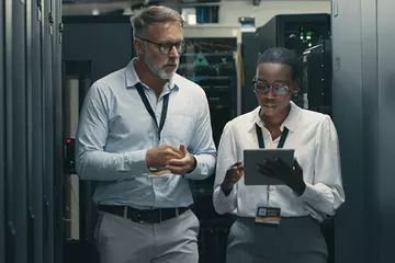 Man and woman walk through server room discussing information security.