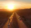 Semi-trucks driving down a divided highway with a sunset in the background.