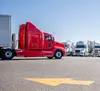 Red truck waiting in busy lot with many other trucks. 
