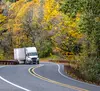 Semi truck driving around a curve surrounded by fall foliage.