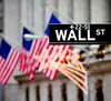 Street sign for "Wall St" in front of American flags.